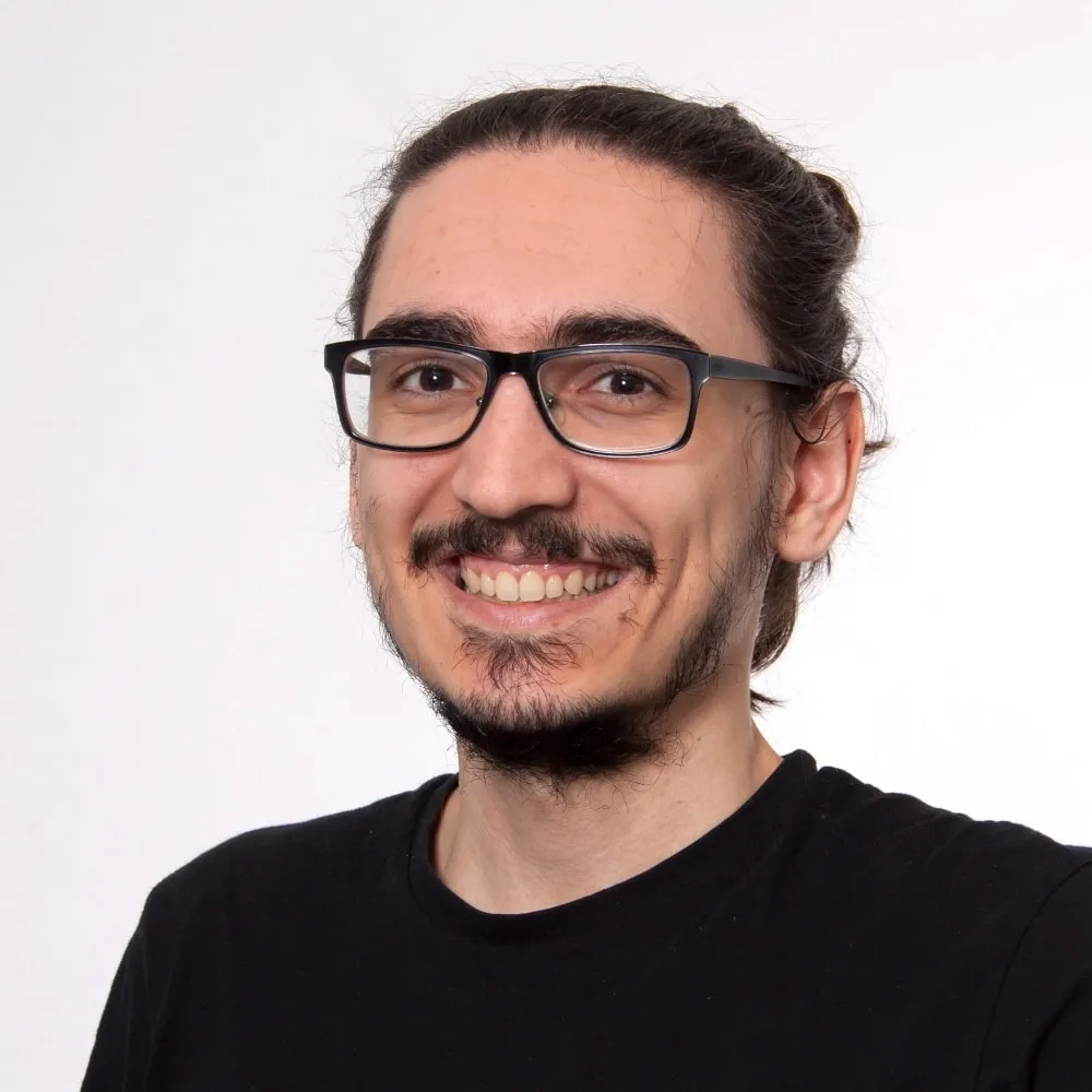 A headshot of me smiling directly at the camera. Long hair bound together, black glasses and a black shirt.